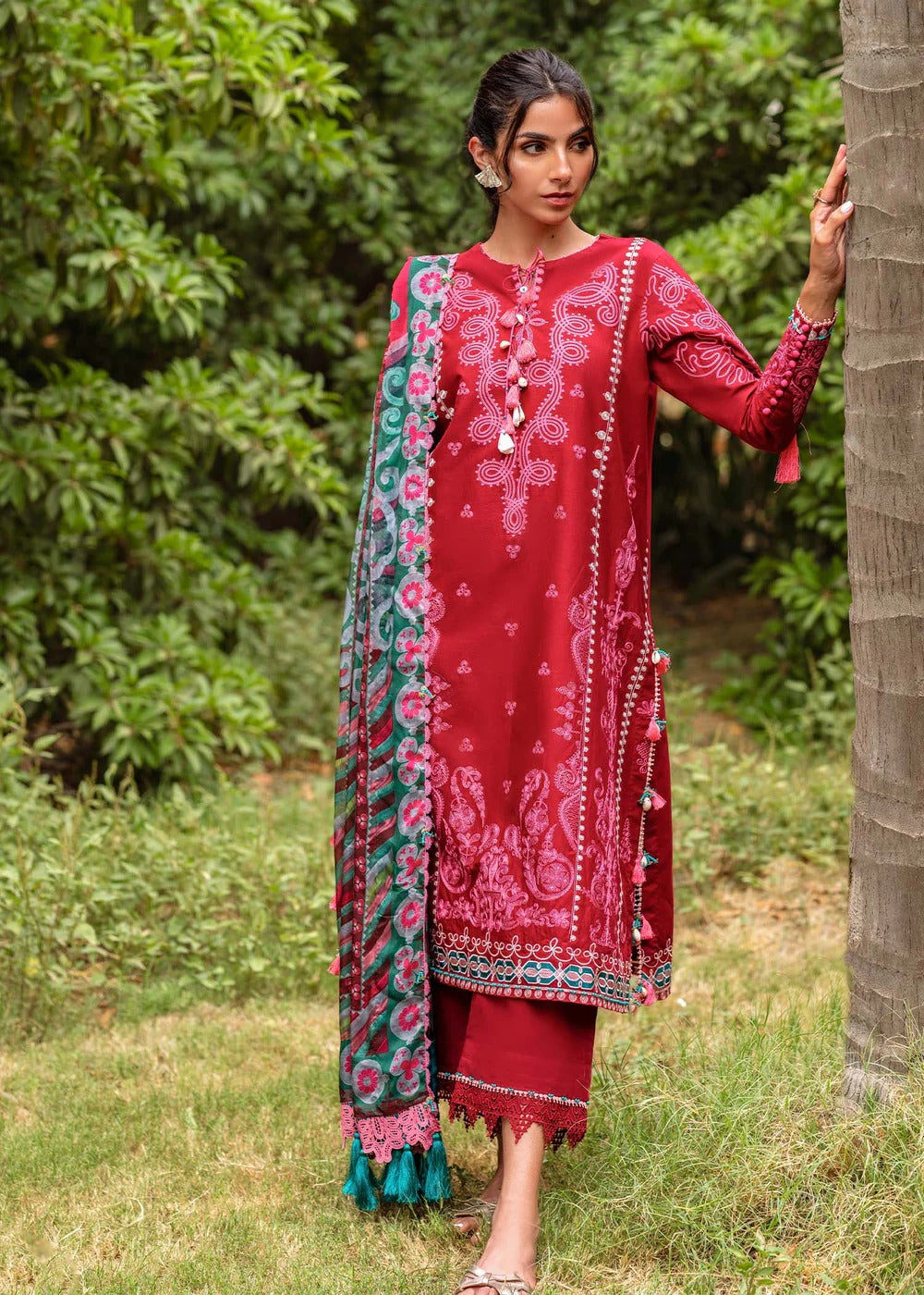Woman in a red traditional outfit with a patterned shawl standing outdoors.