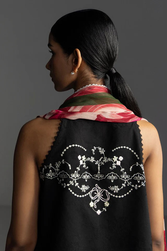 Woman wearing a black sleeveless top with intricate white embroidery, red and green patterned scarf on gray background