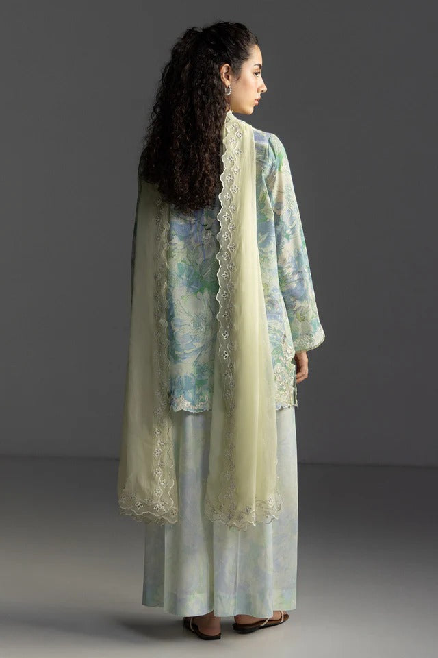 Woman wearing a light green traditional outfit with a floral dupatta against a gray background