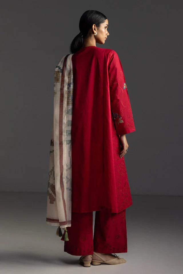 Woman wearing a red traditional outfit with a patterned scarf on a gray background