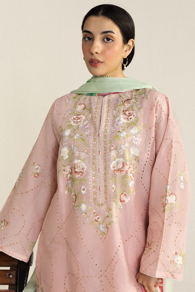 Woman wearing a pink embroidered outfit with a light green scarf against a plain background