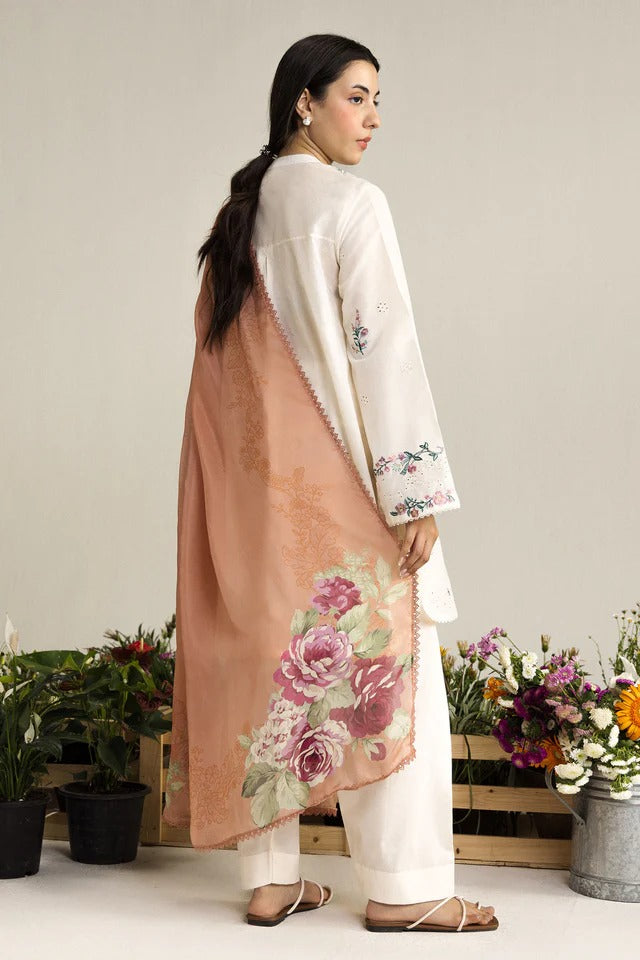 Woman wearing a white outfit with a floral shawl in a minimalistic setting with plants and flowers.