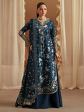 Woman wearing a dark blue embroidered traditional outfit with gold details against a beige curtain background.