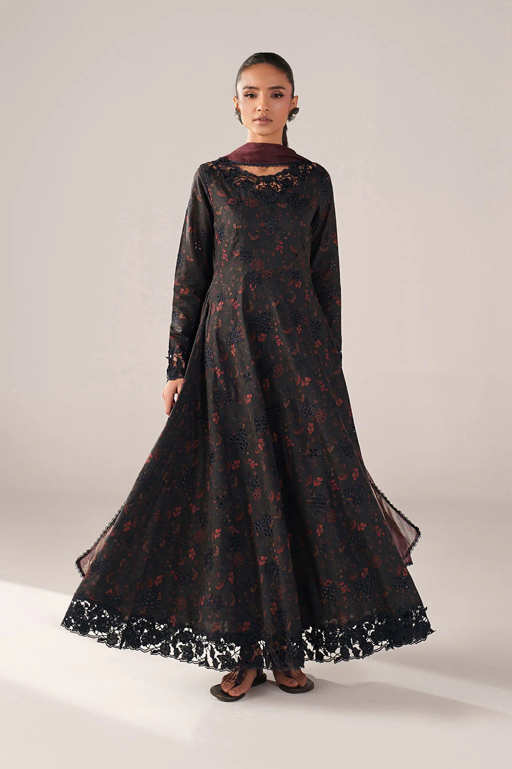 Woman wearing a long black dress with floral patterns on a plain background