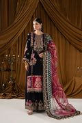 A woman models a traditional South Asian salwar kameez suit in dark navy blue with intricate gold, pink, and red embroidery, paired with a matching patterned dupatta, set against a draped brown curtain background.