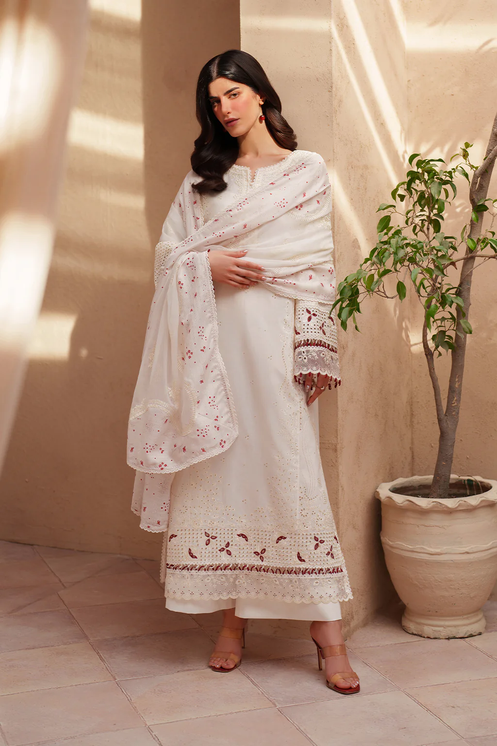 Woman in a white traditional outfit with embroidery standing in a sunlit room.