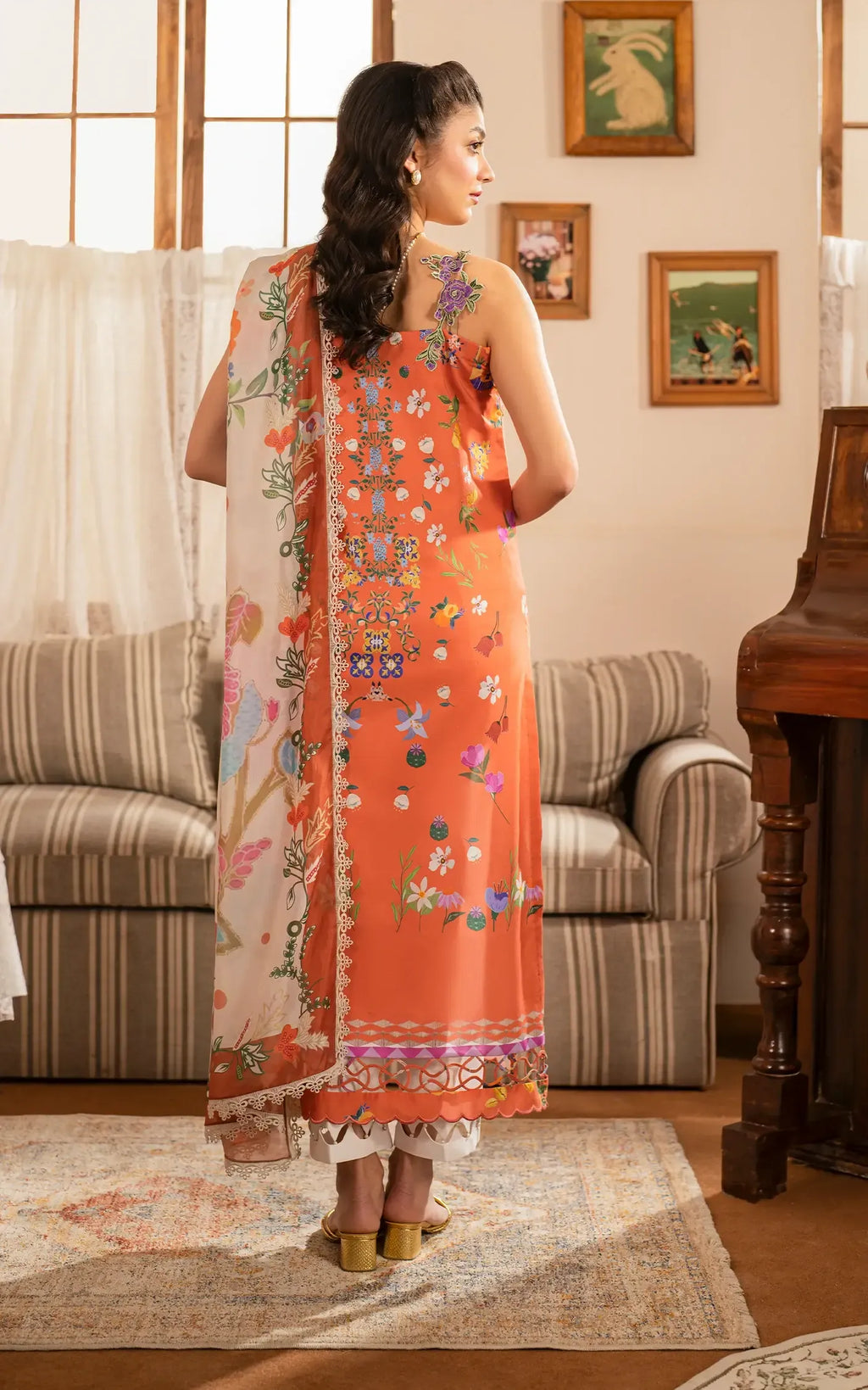 Woman in an orange floral dress standing in a living room.