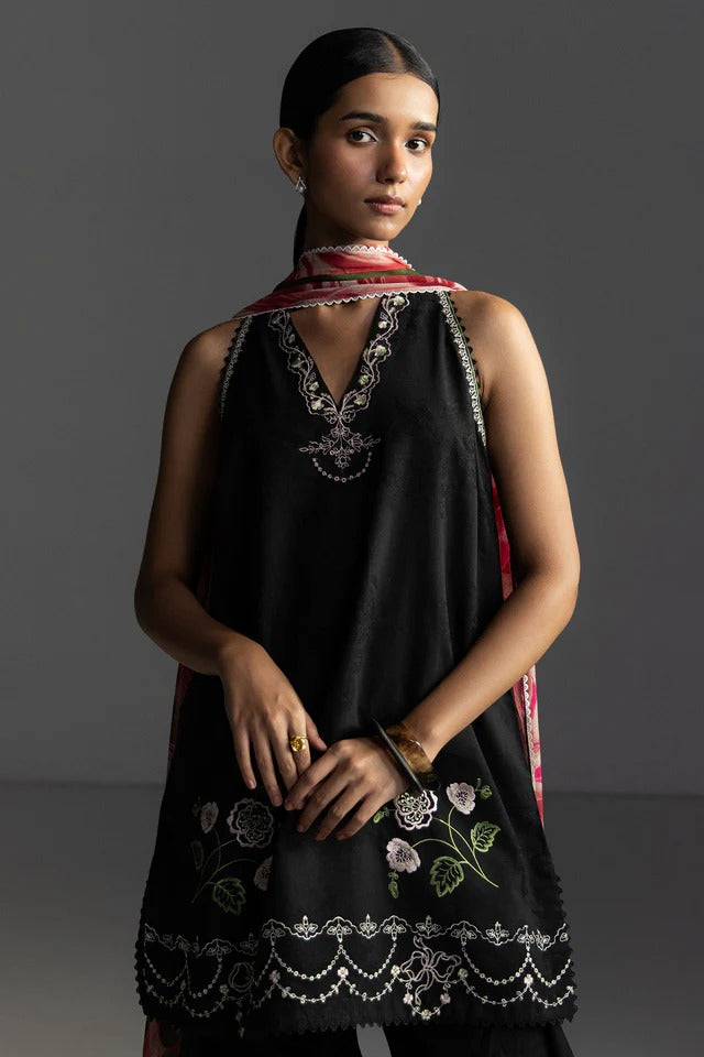 Woman wearing a black embroidered dress with a red and white scarf against a dark background