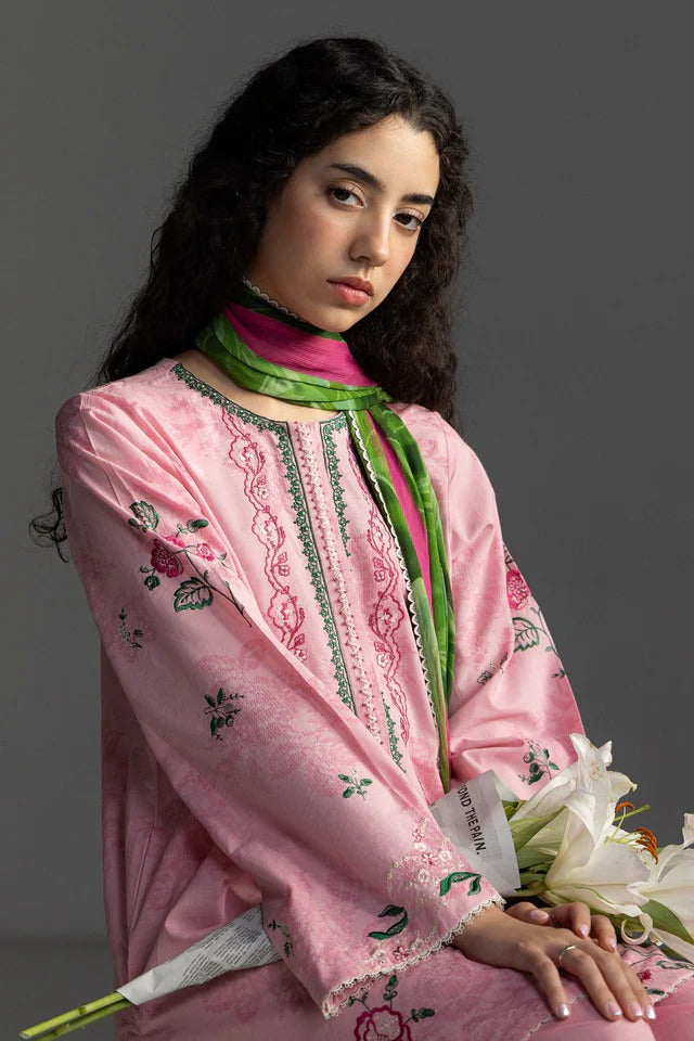 Woman wearing a pink embroidered outfit with a green scarf against a gray background