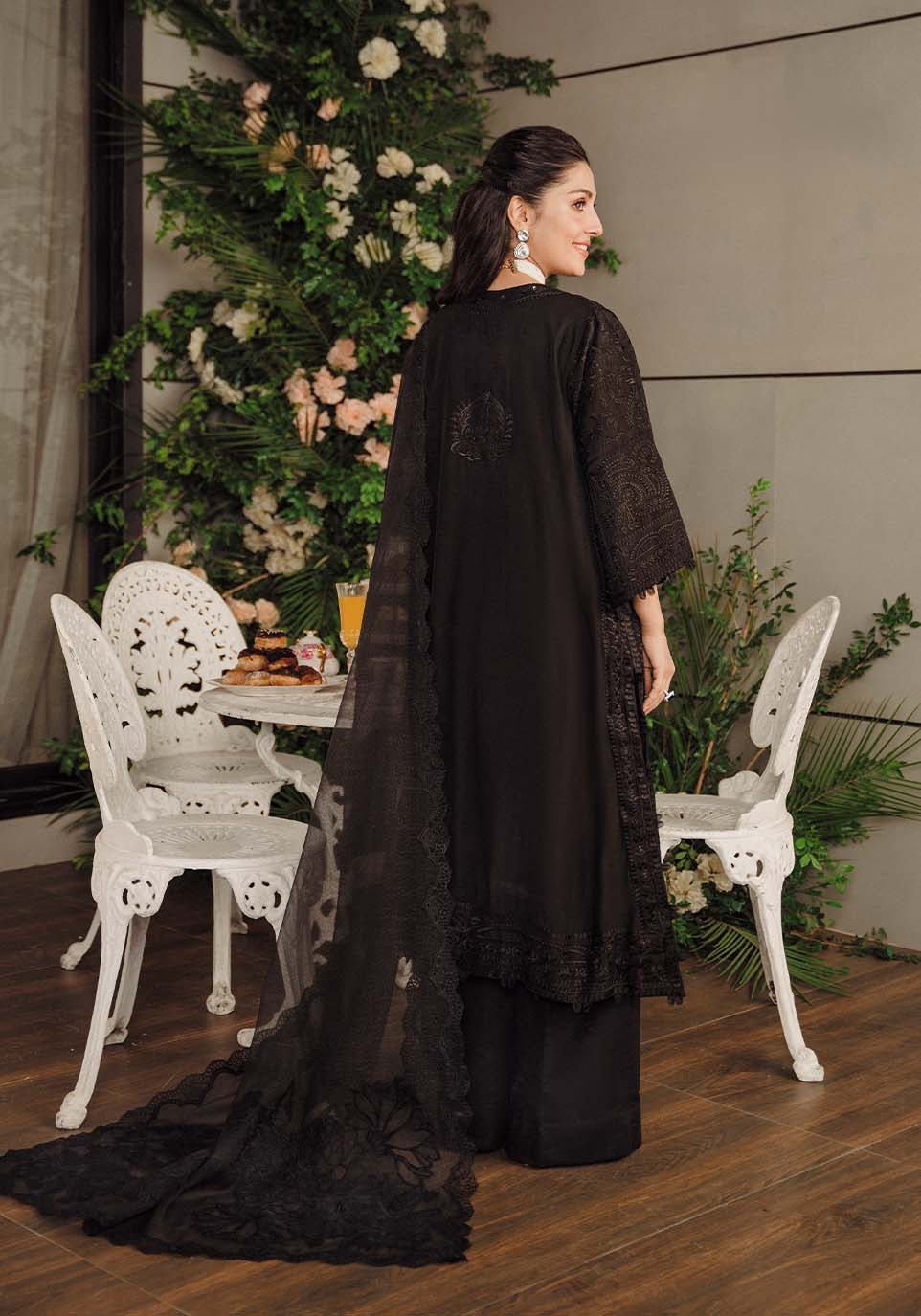 Woman in a black outfit standing in a decorated indoor setting with white chairs and floral arrangements.