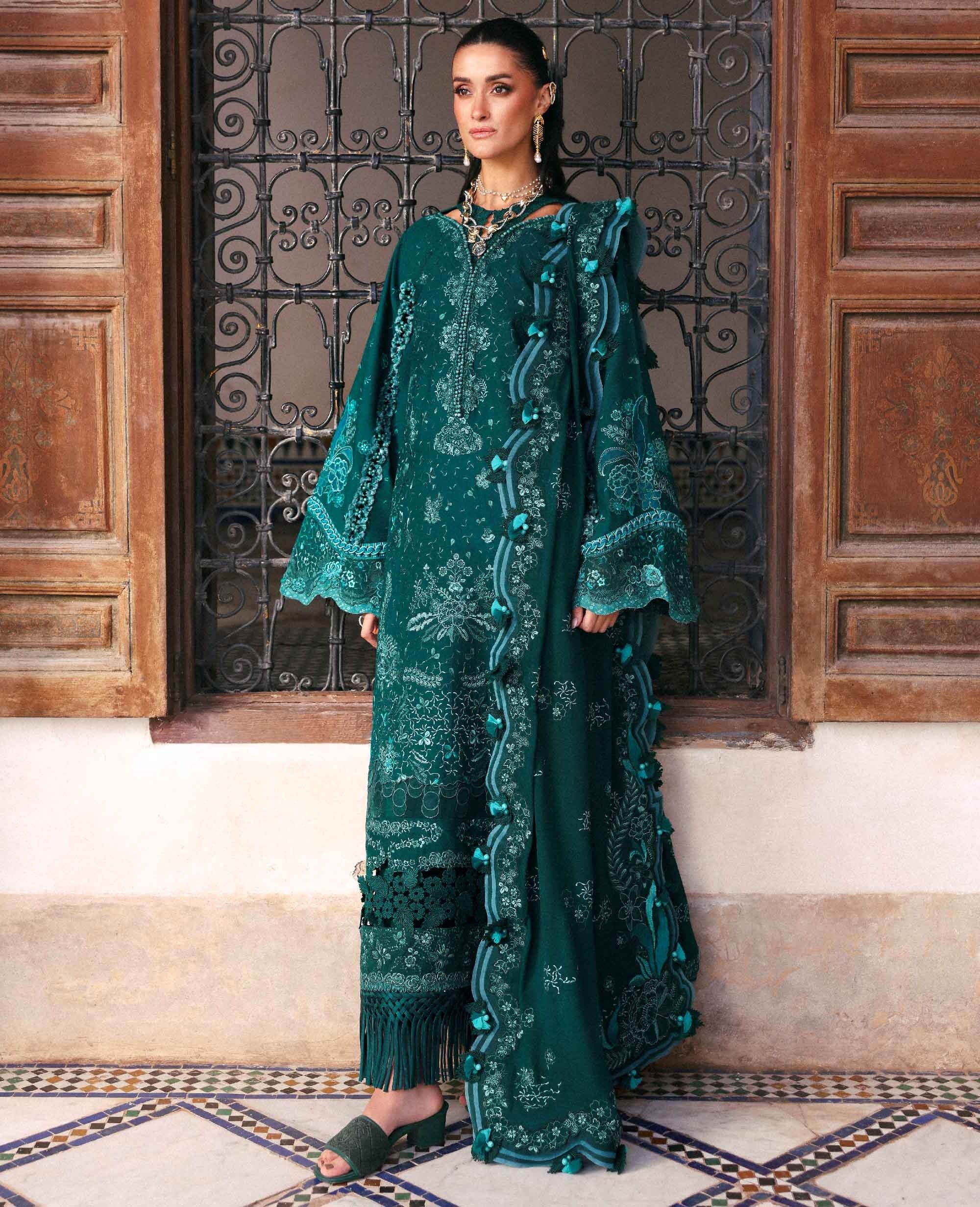 Woman in a teal embroidered dress standing in front of a decorative metal gate.