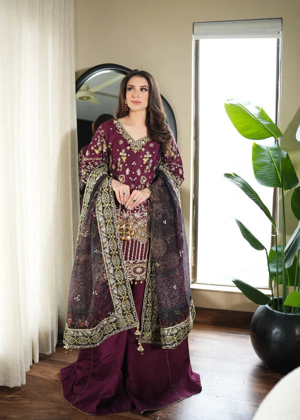 Woman in a traditional purple and gold outfit standing in a room with a mirror and plant.