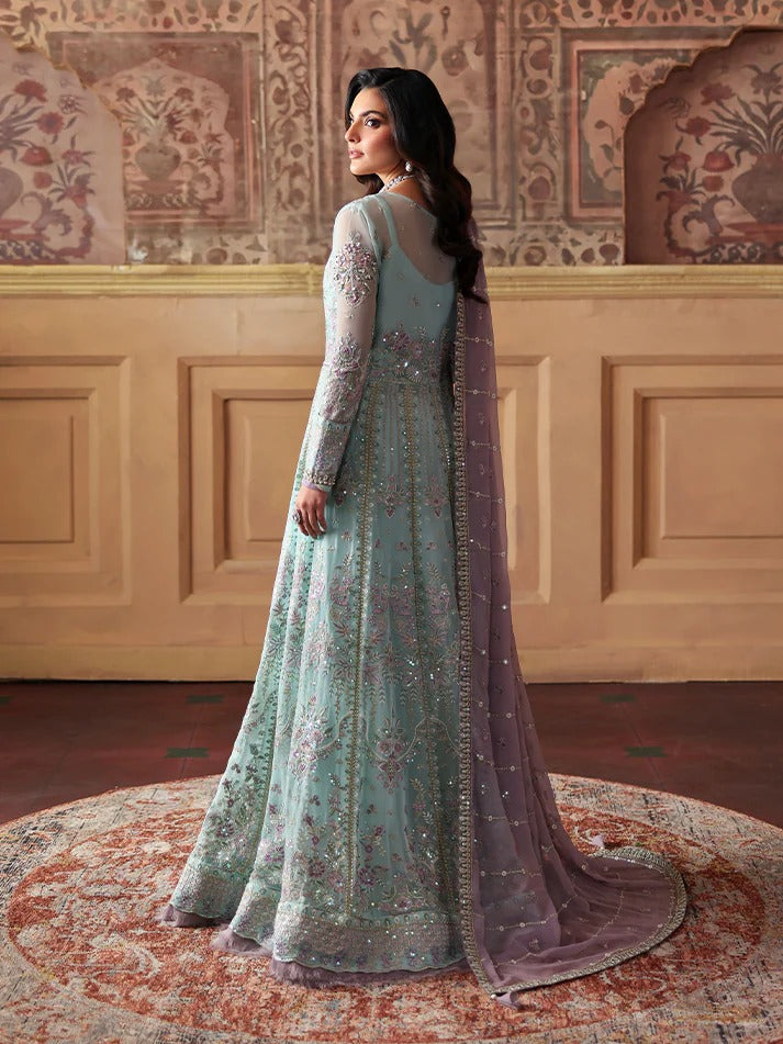 Woman in a light blue embroidered gown with a pink dupatta standing in a decorated room.