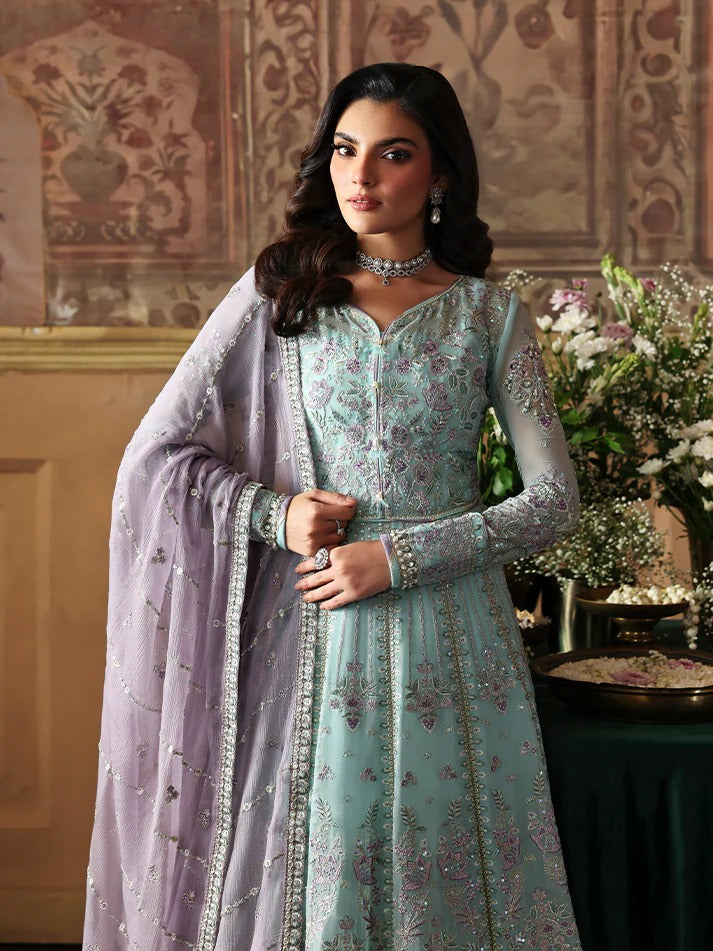 Woman in a light blue embroidered outfit with a matching dupatta, standing in an ornate room.