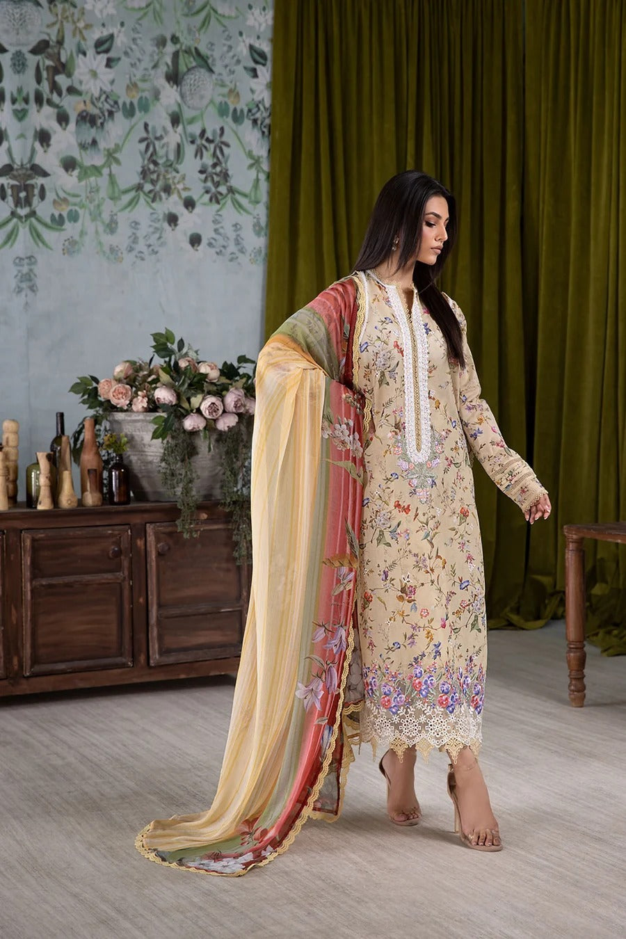 Woman in a floral dress with a long scarf in a room with decorative elements.
