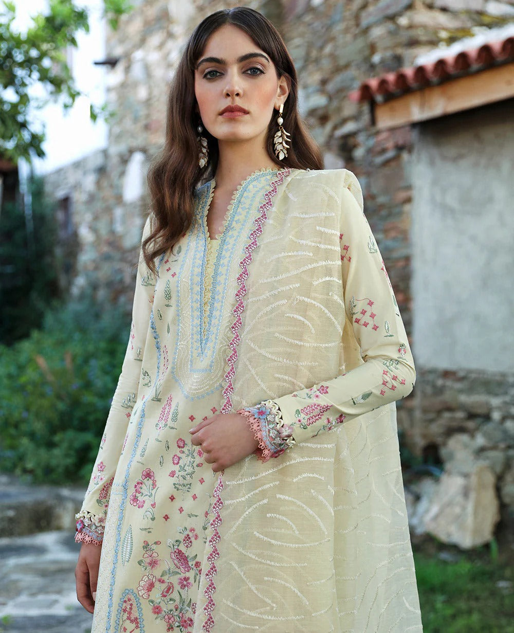Woman wearing a light-colored embroidered traditional outfit with a stone building and greenery in the background