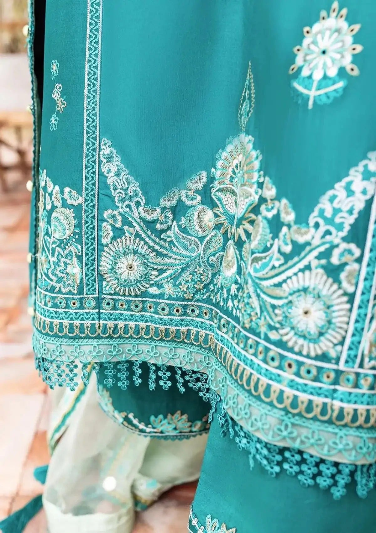 A close-up of a teal green embroidered fabric garment, likely a traditional South Asian outfit, featuring intricate white and silver floral embroidery, border patterns, and a matching sheer dupatta.