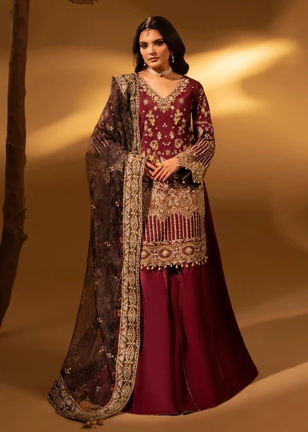 Woman wearing a traditional maroon and gold embroidered outfit with a sheer dupatta against a warm-toned background.