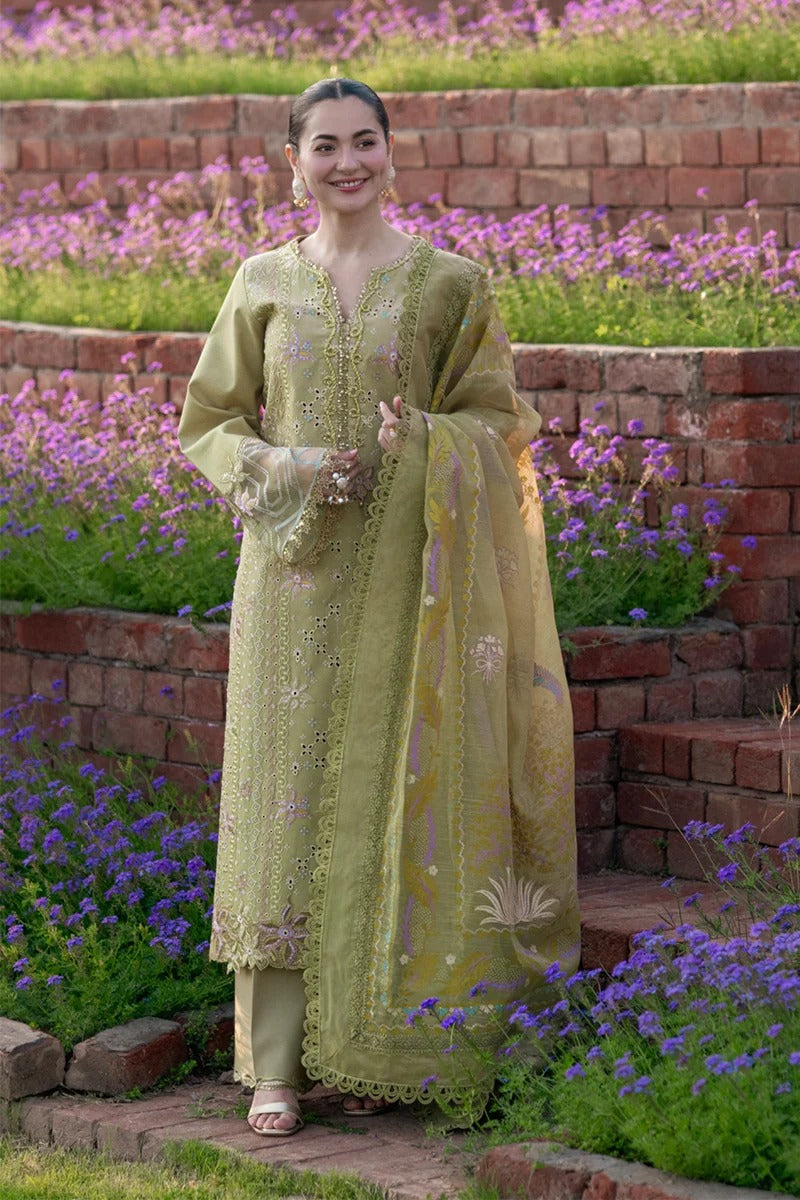 Woman in a green embroidered traditional outfit standing in a garden with flowers and brick steps.
