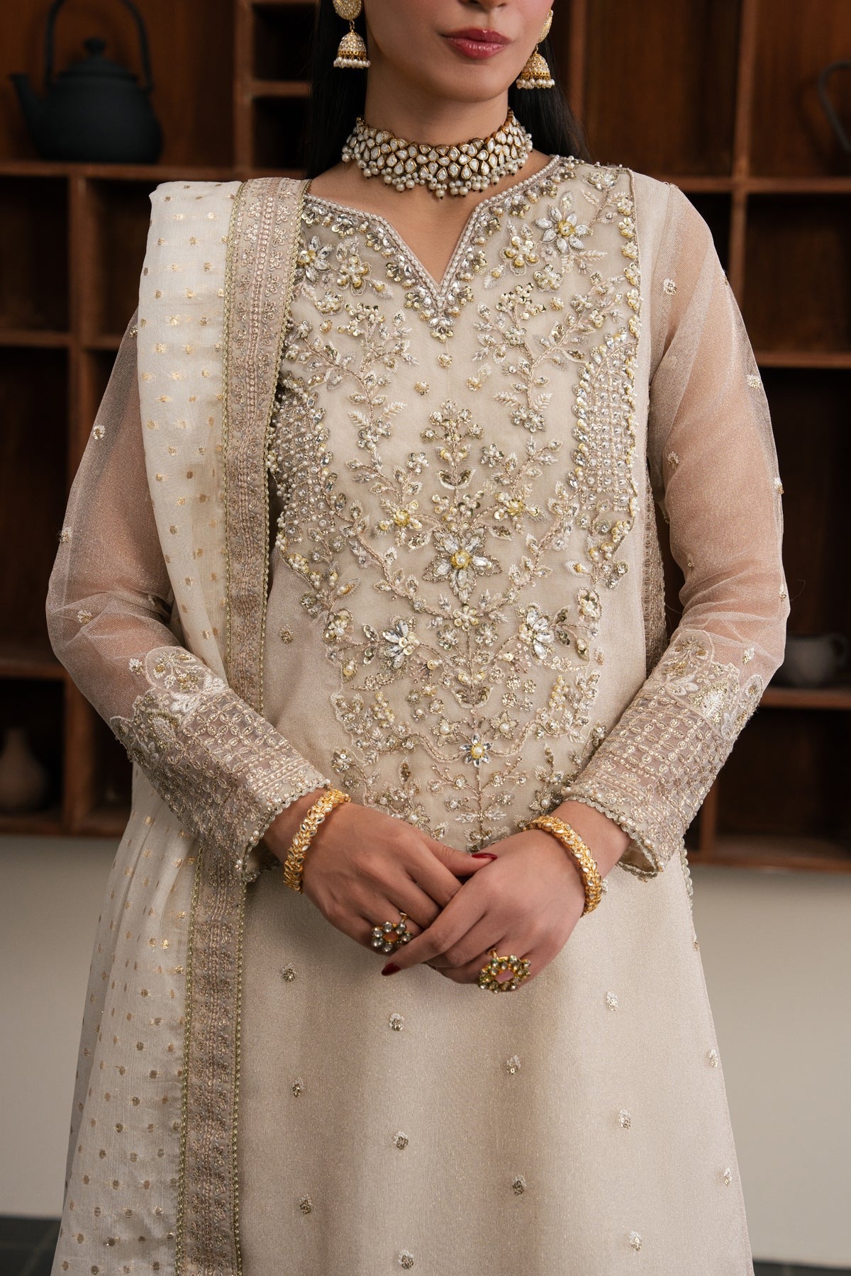A woman wearing a traditional beige embroidered kurta set with a matching dupatta, featuring intricate gold and silver beadwork, styled with gold jewelry.
