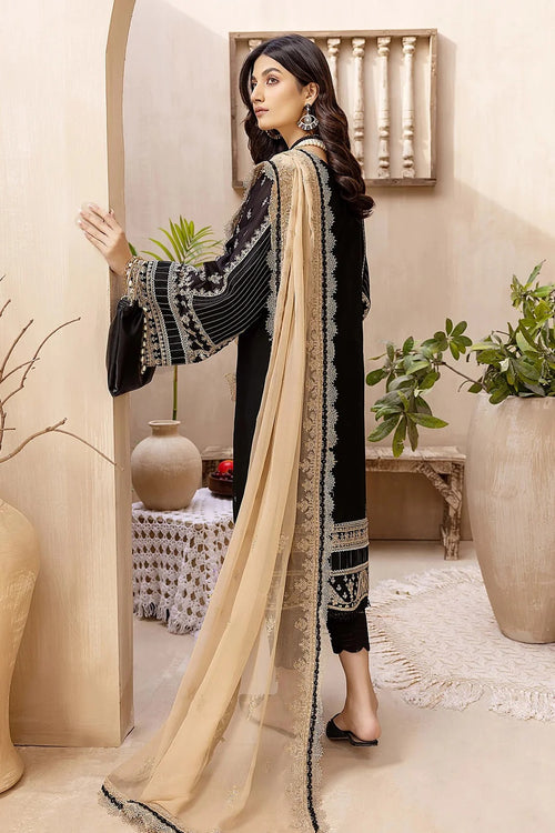 A woman models a black 3-piece salwar kameez suit with intricate silver embroidery, paired with a beige dupatta featuring black borders, in a warm-toned indoor studio setting.