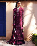 Woman in a traditional purple embroidered outfit standing against a beige wall with a blue door.