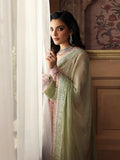 Woman in a light green traditional outfit standing by a window with decorative wall in the background