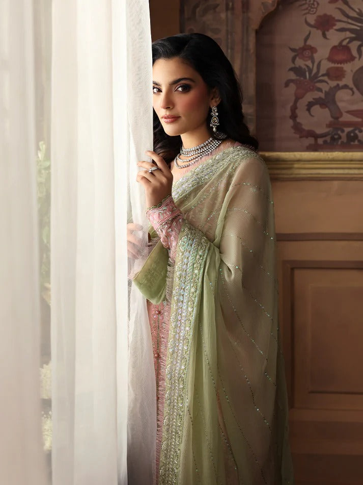 Woman in a light green traditional outfit standing by a window with decorative wall in the background