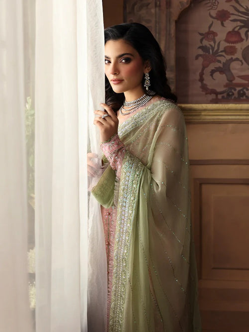 Woman in a light green traditional outfit standing by a window with decorative wall in the background