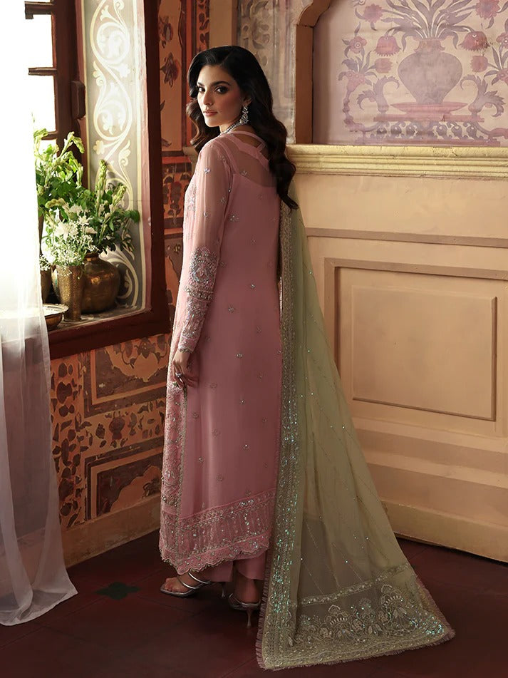 Woman in a pink traditional outfit with a green dupatta standing in an ornate room.