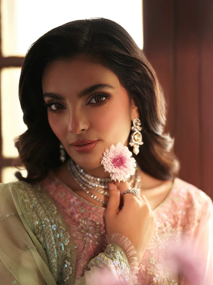 Woman holding a pink flower in front of her face, wearing traditional jewelry.