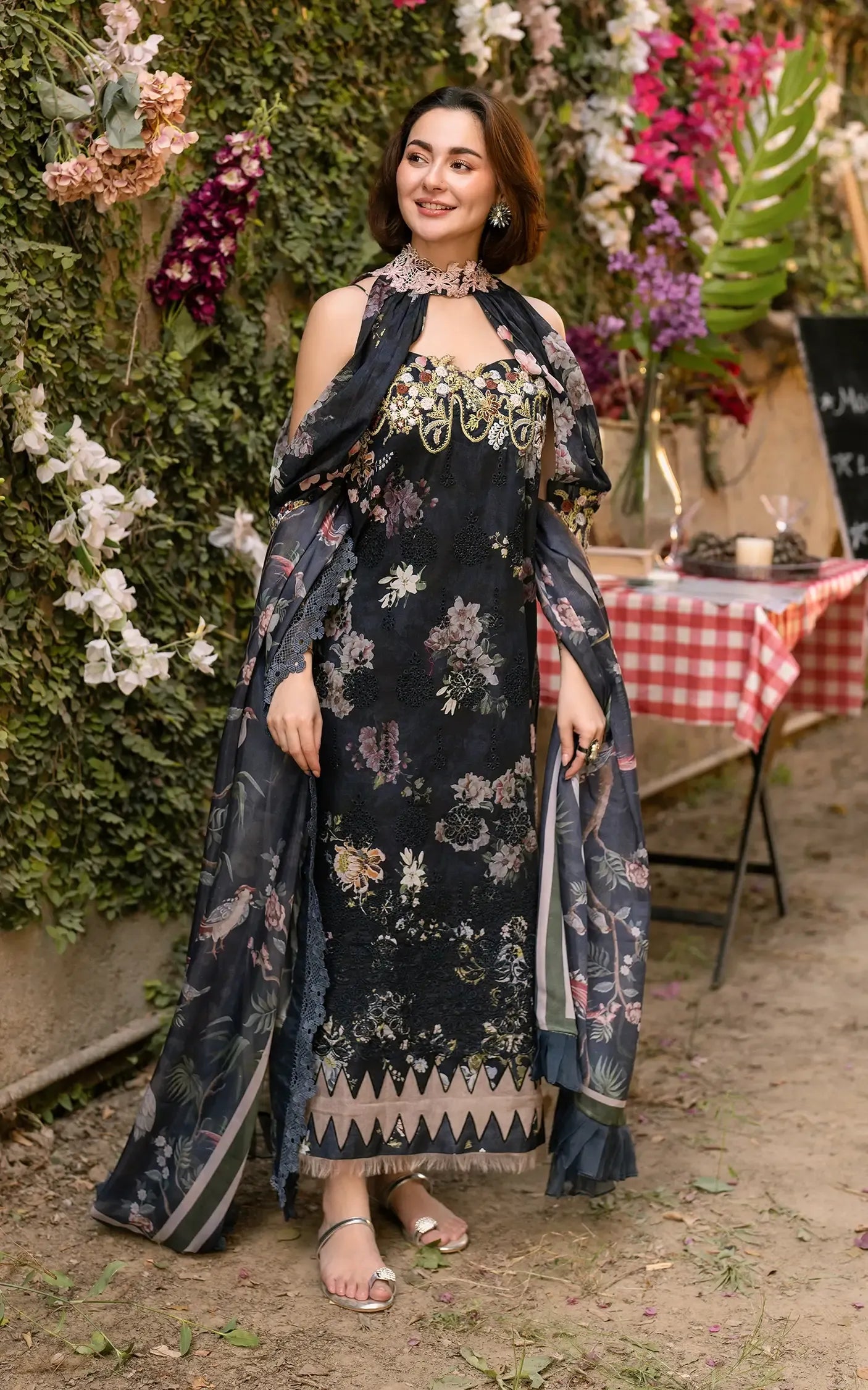 Woman in a floral dress standing outdoors with flowers and a tablecloth in the background