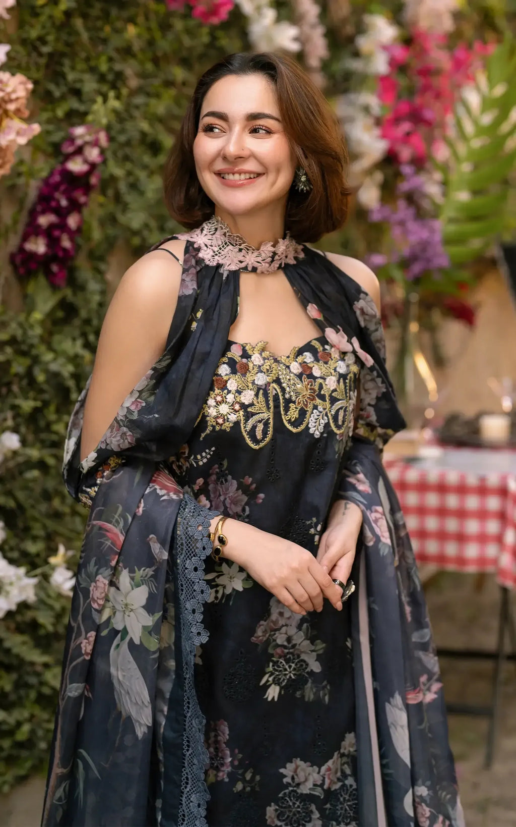 Woman in a floral dress standing in front of decorative flowers and a tablecloth.