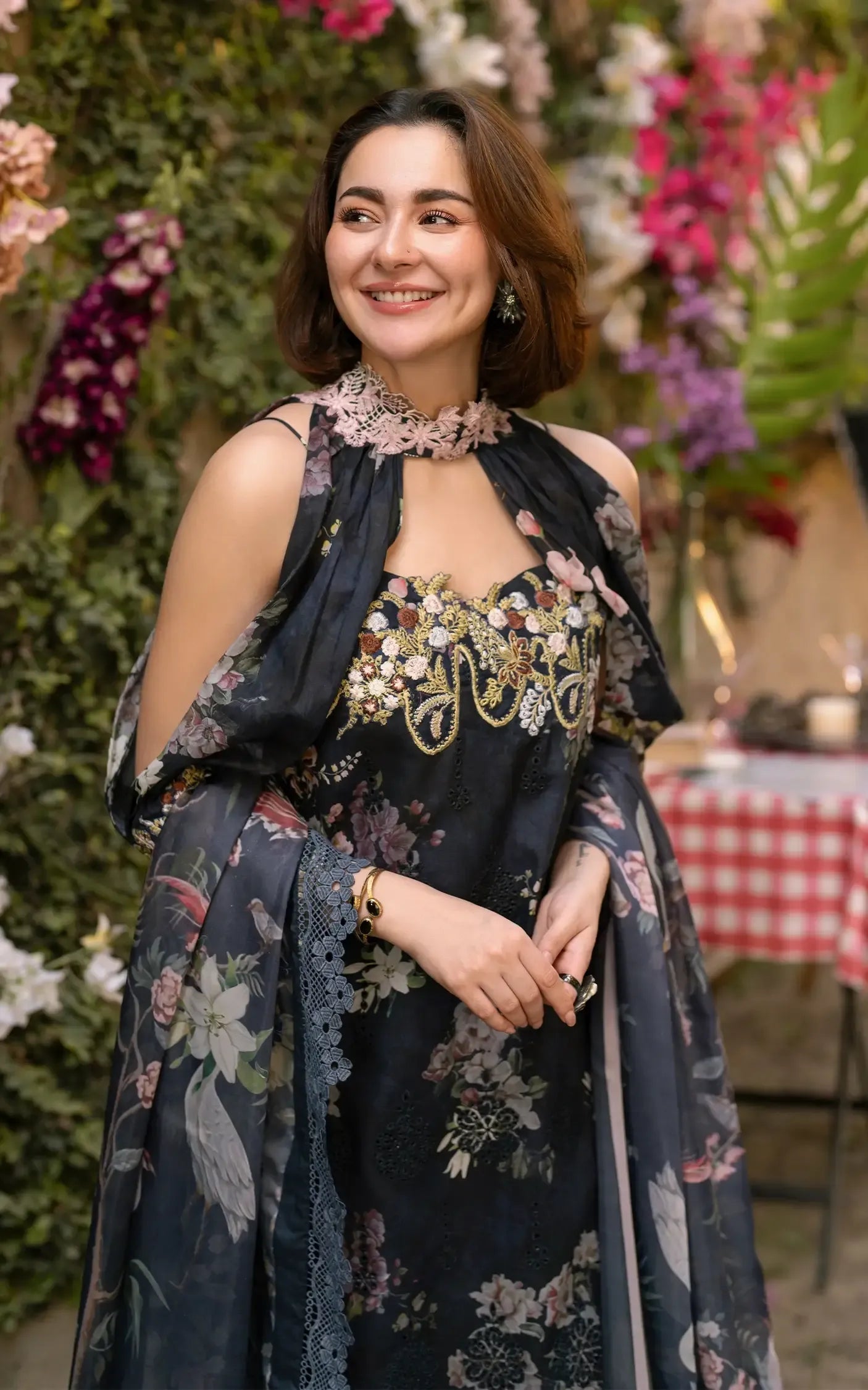 Woman in a floral dress standing in front of decorative flowers and a tablecloth.