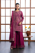 A woman models a traditional three-piece salwar kameez suit in deep magenta with intricate gold embroidery and a matching dupatta, standing in front of a wooden grid screen.