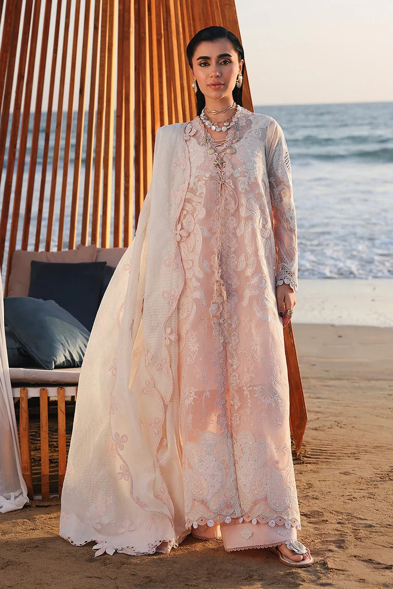 Woman in a light pink embroidered dress standing on a beach with ocean view.