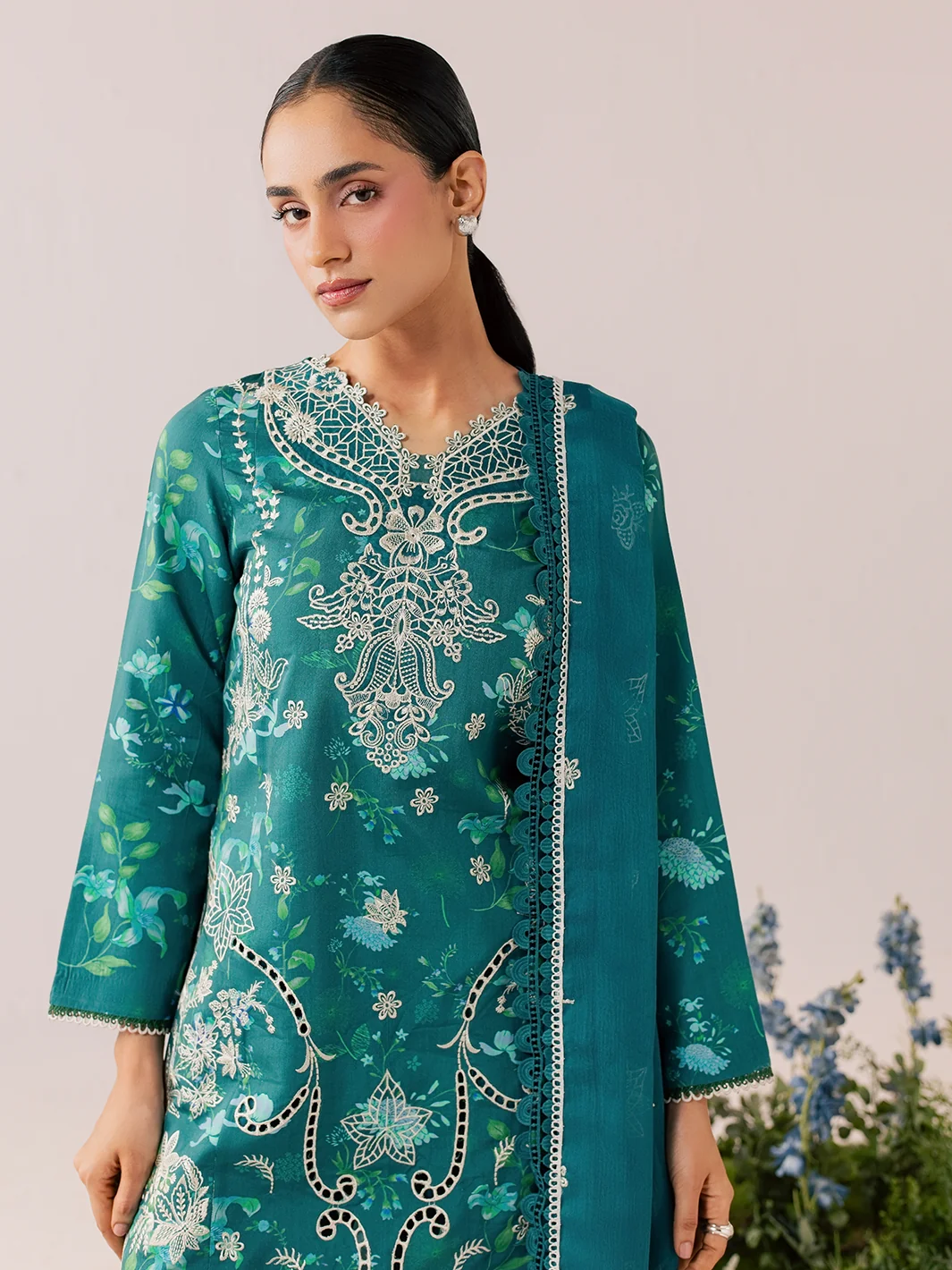A woman modeling a teal green ethnic kurta with intricate white and silver floral embroidery, paired with a matching dupatta, set against a soft beige background.