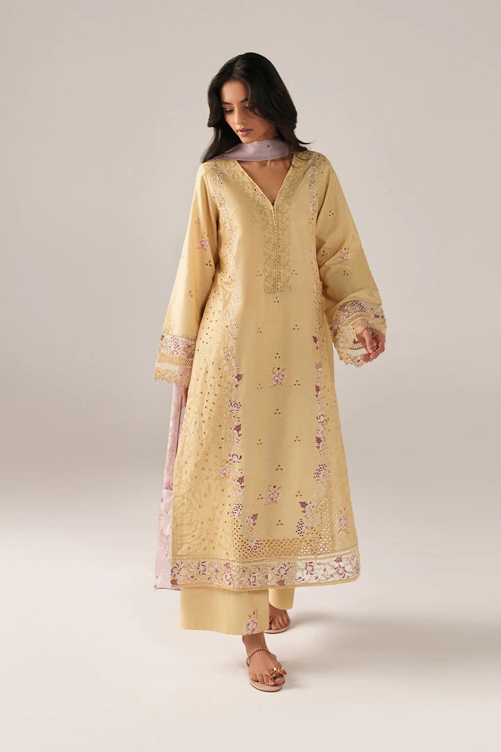 A woman modeling a traditional long kurta in pale yellow with delicate floral embroidery and a matching dupatta, set against a plain light beige studio background.