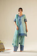 Woman wearing a light blue embroidered outfit with dark blue patterns on a neutral background