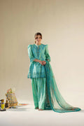 Woman in a green and blue traditional outfit with a matching dupatta on a beige background