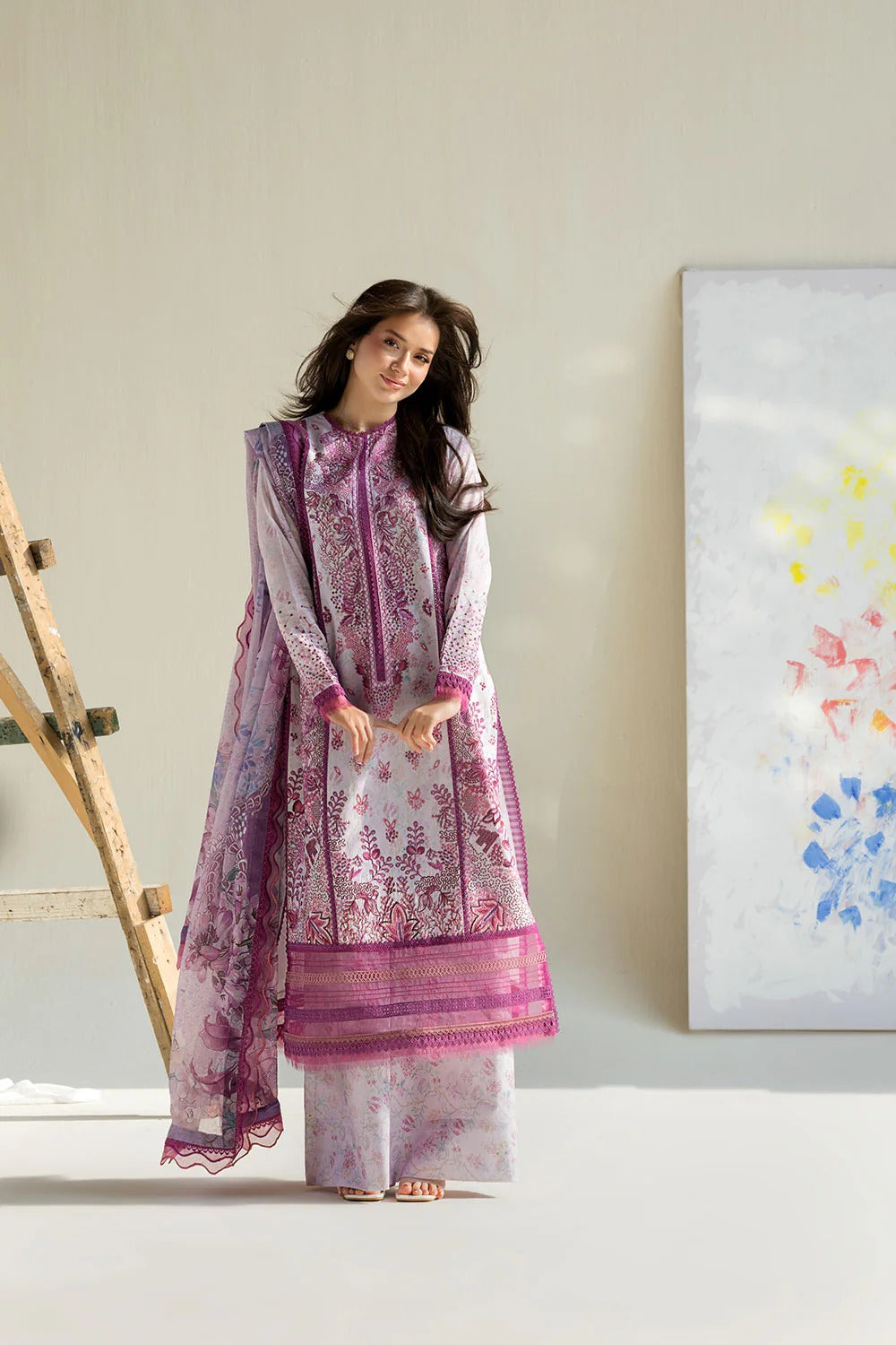 Woman in a light purple traditional outfit standing in a room with a painting on the wall.