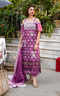 Woman in a pink and purple floral dress standing outdoors with plants and furniture in the background