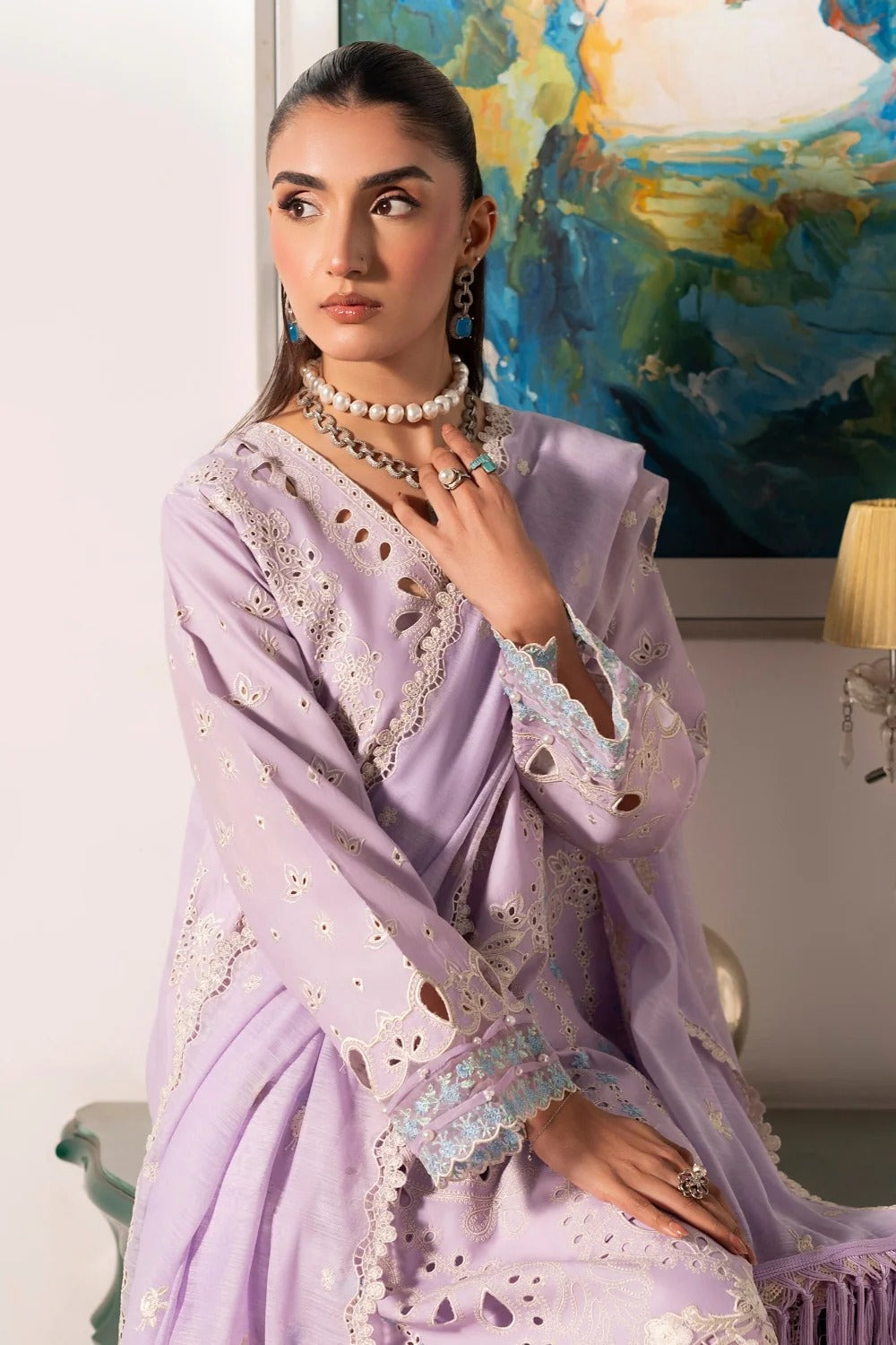 Woman wearing a lavender saree with intricate designs in a room with a colorful painting on the wall.