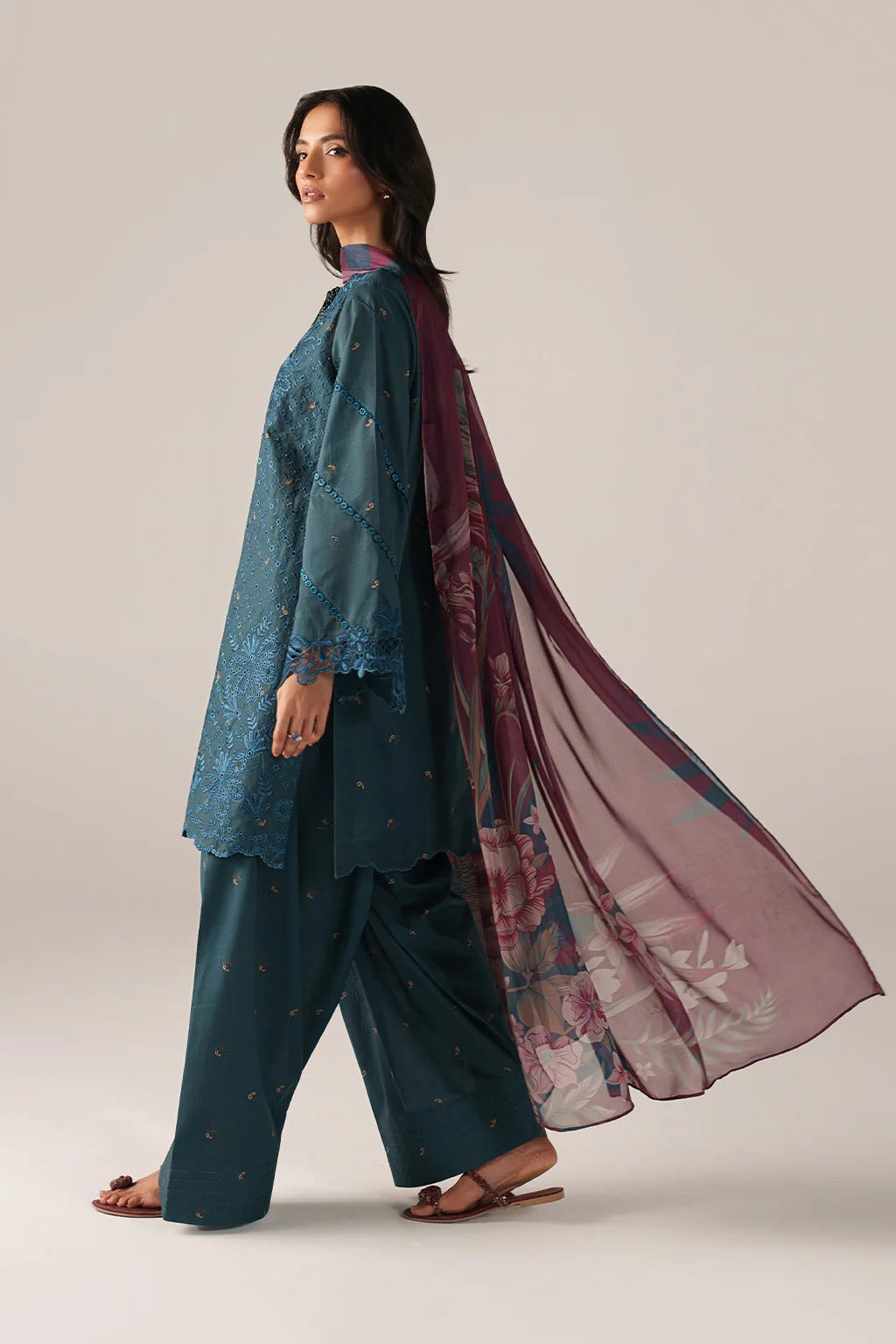 Woman wearing a teal outfit with a floral scarf on a plain background