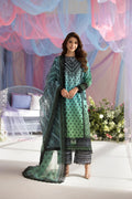 Woman in a green and black traditional outfit standing in a decorated room with colorful drapes and flowers.