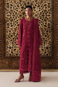 A woman models a deep magenta embroidered traditional outfit with a matching dupatta, standing in front of a large patterned oriental rug.