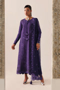 A woman models a long-sleeved purple embroidered kurta with a matching sheer dupatta, standing between two stone pillars against a light beige background.