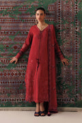 A woman models a traditional red embroidered kurta set with a matching dupatta, standing against a patterned green and red rug.