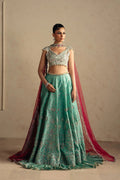 A woman models an ornate traditional Indian lehenga choli set. The outfit features a mint green embroidered skirt with floral patterns, a matching embroidered crop top, and a deep red dupatta draped over her shoulder and floor.