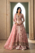 A woman models a traditional pink Indian lehenga choli with intricate gold embroidery, standing in a grand arched doorway.